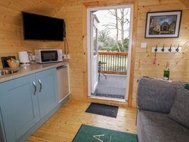 A small wooden kitchen area with blue cabinets a microwave kettle and a wall mounted TV next to a door opening to a balcony with trees visible and a gray sofa on the right at Hazel in Dungiven Londonderry