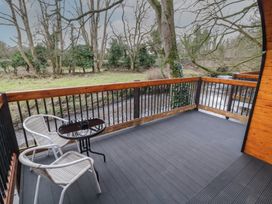 A balcony with two chairs and a round table overlooking a river and trees at Hazel in Dungiven Londonderry