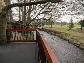 A wooden deck with railing beside a flowing river and trees at Juniper in Dungiven Londonderry