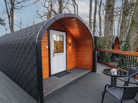 An outdoor pod with a white door and wooden interior on a deck with two black chairs and a round glass table at Birch in Dungiven Londonderry