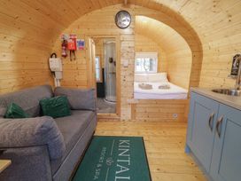 An interior of a wooden cabin with a gray sofa green pillows a bed with folded towels a small bathroom and a kitchenette at Kintail Resort Dungiven Londonderry