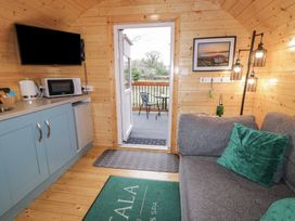 A small wooden cabin interior with a kitchenette including microwave and kettle a gray sofa with green cushions a door leading to a balcony with chairs and a table Birch Dungiven Londonderry
