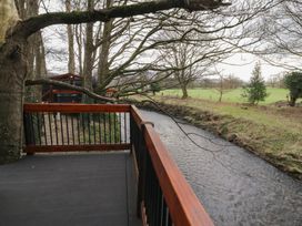 A wooden deck overlooking a river with trees and grass in the background at Yew in Dungiven Londonderry