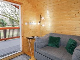 A room with wooden walls featuring a grey sofa with green cushions a small side table with reading materials and a floor lamp next to an open door leading to an outdoor area at Yew in Dungiven Londonderry