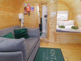A wooden cabin interior with a gray sofa with green pillows a bed with folded towels and a shower enclosure at Yew in Dungiven Londonderry