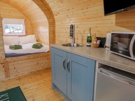 A wooden cabin interior with a bed with white bedding and green towels next to a blue kitchen cabinet with a sink microwave and mini fridge at Yew in Dungiven Londonderry