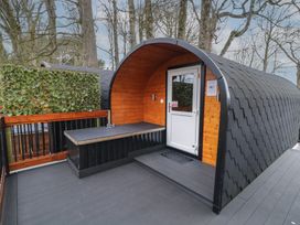 An outdoor pod cabin with wooden walls a white door and a black tiled curved roof on a grey deck with trees in the background at Elm in Dungiven Londonderry