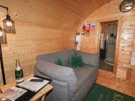 A small wooden room with a gray sofa with two green pillows a wooden side table with a bottle and papers a door leading to a bathroom with a shower at Elm in Dungiven Londonderry