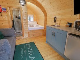 A small wooden room with a kitchenette a gray sofa a bed with white linens and a shower visible at Kintala Resort and Spa