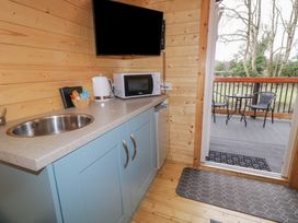 A kitchenette with a sink microwave kettle and a small fridge next to a door leading to a deck with a table and two chairs at Elm in Dungiven Londonderry