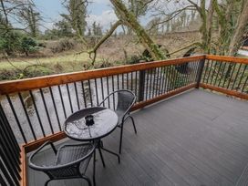 A balcony with a round glass table and two black chairs overlooking a river with trees at Hawthorn in Dungiven Londonderry