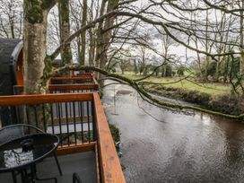 A balcony with a round table and chairs overlooking a river with trees at Hawthorn in Dungiven Londonderry