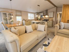 An open plan living room and kitchen with beige sofas dining table and kitchen island at Debonair Lodge in Three Lochs Holiday Park near Glenluce