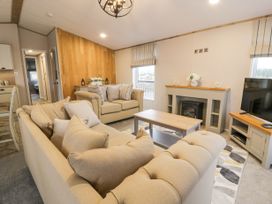 A living room with beige sofas and a coffee table with a television and fireplace at Debonair Lodge in Three Lochs Holiday Park near Glenluce