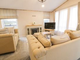 A living room with beige sofas a fireplace a television and large windows at Debonair Lodge in Three Lochs Holiday Park near Glenluce