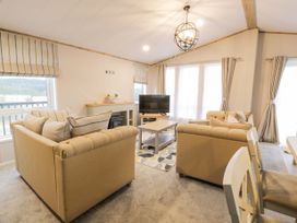 A living room with two beige sofas a wooden coffee table and a television at Debonair Lodge in Three Lochs Holiday Park near Glenluce