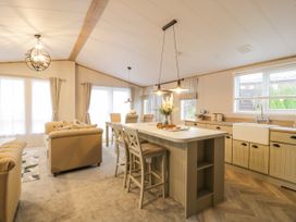 An open living room and kitchen with beige sofas a kitchen island and dining table at Debonair Lodge in Three Lochs Holiday Park near Glenluce
