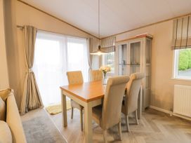 A dining room with a wooden table four upholstered chairs glass cabinet and striped curtains at Debonair Lodge in Three Lochs Holiday Park near Glenluce