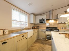 A kitchen with beige cabinets a white farmhouse sink a microwave oven and a stove at Debonair Lodge in Three Lochs Holiday Park near Glenluce