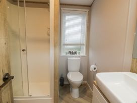 A bathroom with a shower, toilet, sink, and window with blinds at Debonair Lodge in Three Lochs Holiday Park near Glenluce
