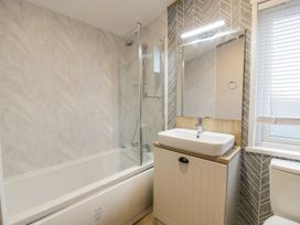 A bathroom with a bathtub shower combination a sink with cabinet a mirror and a window with blinds at Debonair Lodge in Three Lochs Holiday Park near Glenluce