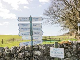 A signpost with multiple directional signs next to a stone wall and tree in a rural area at Debonair Lodge in Three Lochs Holiday Park near Glenluce
