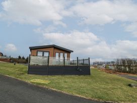 A wooden lodge with glass railings on a grassy hill with other lodges in the background at Debonair Lodge in Three Lochs Holiday Park near Glenluce