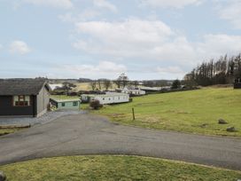 A paved road with grass and several small buildings and caravans in a rural area at Debonair Lodge in Three Lochs Holiday Park near Glenluce