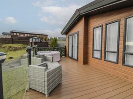 An outdoor deck with wicker chairs and a hot tub next to a wooden building at Debonair Lodge in Three Lochs Holiday Park near Glenluce