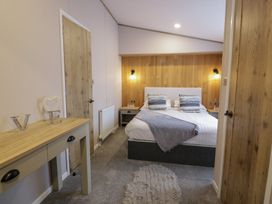 A bedroom with a double bed two pillows bedside tables and a wooden console table at Debonair Lodge at Three Lochs Holiday Park near Glenluce