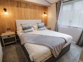A bedroom with a double bed bedside tables lamps and a large window with curtains at Debonair Lodge in Three Lochs Holiday Park near Glenluce