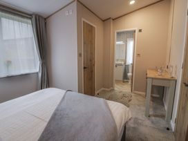 A bedroom with a bed a window with curtains a small table and an open door to a bathroom at Debonair Lodge in Three Lochs Holiday Park near Glenluce