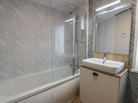 A bathroom with a bathtub and glass shower screen next to a sink with cabinet and mirror at Debonair Lodge in Three Lochs Holiday Park near Glenluce