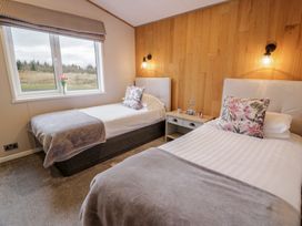 A bedroom with two single beds a nightstand a window and wooden wall paneling at Debonair Lodge in Three Lochs Holiday Park near Glenluce