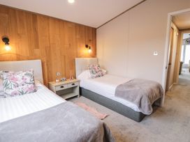 A bedroom with two single beds a bedside table and wall lamps at Debonair Lodge Three Lochs Holiday Park near Glenluce