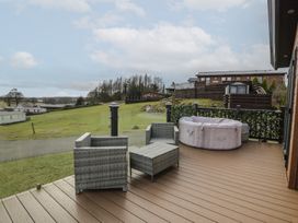 A wooden deck with outdoor wicker furniture and a round inflatable hot tub on a grassy hillside at Debonair Lodge in Three Lochs Holiday Park near Glenluce