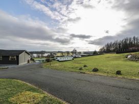 A road with grass fields and houses near a body of water at Debonair Lodge in Three Lochs Holiday Park near Glenluce