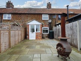 A paved backyard with a white door and window on a brick house and a metal outdoor fireplace at 3 Victoria Cottages in Heacham