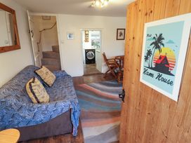 A sitting room with a sofa covered with a blue throw and cushions a wooden door with a poster a wooden table and chairs and a doorway leading to a kitchen at 3 Victoria Cottages in Heacham