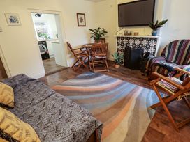 A living room with a patterned rug a round wooden table with chairs a sofa and a wall-mounted television at 3 Victoria Cottages Heacham