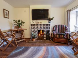 A living room with a patterned fireplace a fire a wall mounted tv wooden chairs a round wooden table and a striped armchair at 3 Victoria Cottages in Heacham