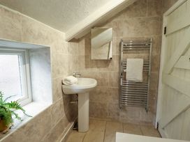 A bathroom with a pedestal sink, mirror, towel rack with towel, window with plant and a white wooden door at 3 Victoria Cottages in Heacham