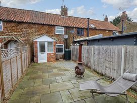 A backyard with stone paving a metal chiminea a lounge chair a wooden fence and a brick house at 3 Victoria Cottages in Heacham
