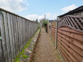 A narrow gravel pathway between two wooden fences with a mossy brick base on one side at 3 Victoria Cottages in Heacham