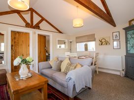 A living room with a gray sofa and wooden coffee table with flowers a dining table with chairs and wood beams on ceiling at Hillview in Stottesdon near Cleobury Mortimer