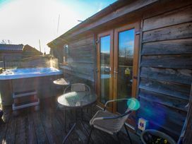 An outdoor wooden deck with a hot tub a glass table and wicker chairs at Hillview in Stottesdon near Cleobury Mortimer