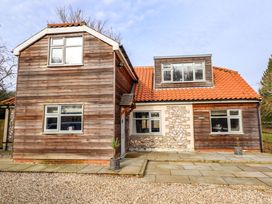 A wooden house with tiled roof gravel driveway and potted plants at Natterjacks in Syderstone