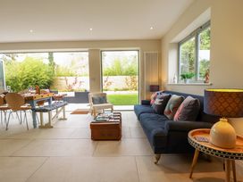 A living room with a navy sofa and cushions a small chair a wooden table with a lamp and a dining table with chairs and bench at Natterjacks in Syderstone