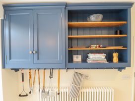 Blue wall-mounted kitchen cabinets with closed doors on the left and open shelves on the right holding a glass bowl books and wooden items kitchen utensils hanging below and an oven mitt on a radiator at Natterjacks Syderstone