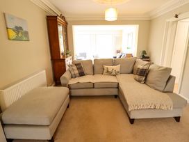 A living room with a beige sectional sofa with cushions an ottoman a wooden cabinet and a painting at Natterjacks in Syderstone